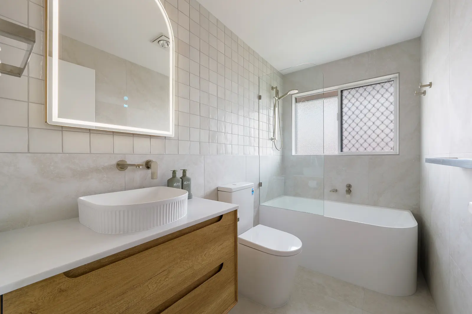 Light-filled bathroom with bath, timber vanity and fluted basin